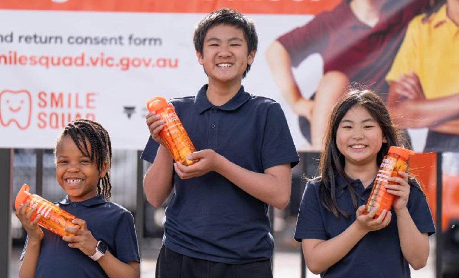 Three school children smiling at camera holding drink bottles