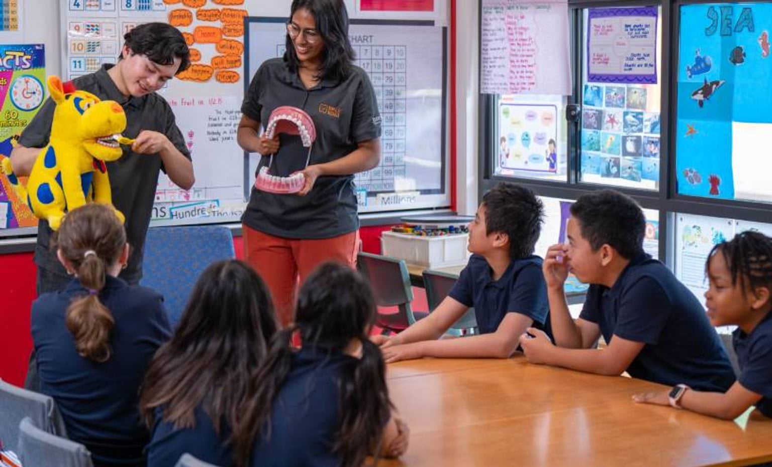 Smile Squad staff in classroom showing students how to brush teeth