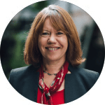 A smiling woman with brown hair, dressed in a red top and navy blazer.