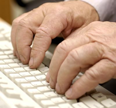 A close-up view of an older man’s hands on a computer keyboard.